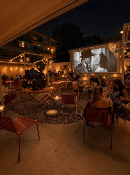 Guests watching an outdoor film screening at night among string lights and candles